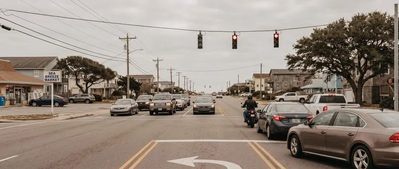 Motorcyclist and cars waiting at a red light on a small coastal-town intersection