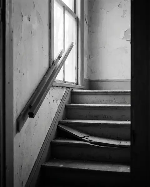 Worn wooden staircase with a broken step and a loose handrail