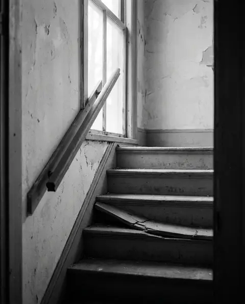 Worn wooden staircase with a broken step and a loose handrail