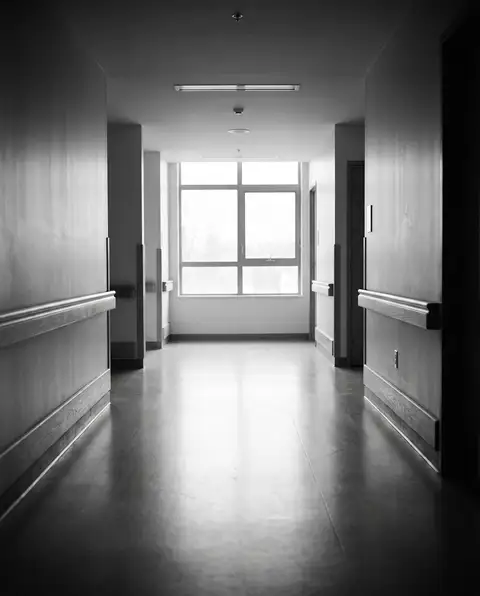 Quiet, empty hospital rehabilitation corridor with soft daylight from a window at the far end